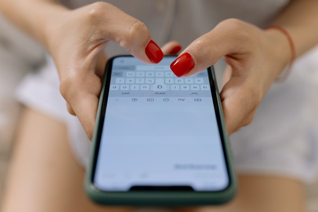 Close-up image of hands with red nails typing on a smartphone screen, showcasing modern technology.