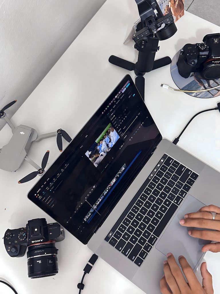 Hands editing aerial footage on laptop with camera, drone, and stabilizer.